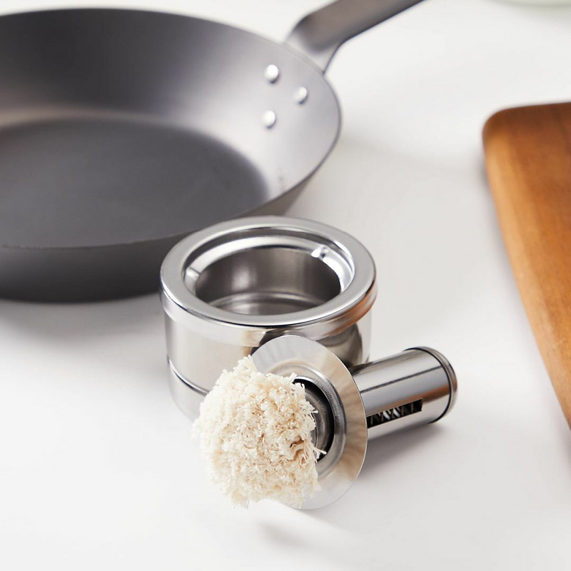 Freiz Stainless Steel Oil Basting Set placed next to a frying pan and wooden cutting board.
