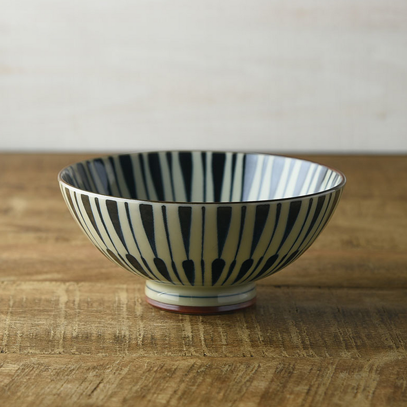 Side view of a traditional Japanese bowl with black Tokusa patterns against a white background, placed on a wooden tabletop.