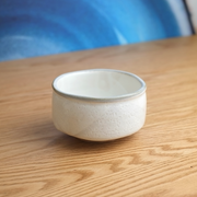 A rustic Yamaman Kohiki-style matcha bowl (chawan), featuring a soft white slip glaze over a darker clay body, with an unglazed foot.

