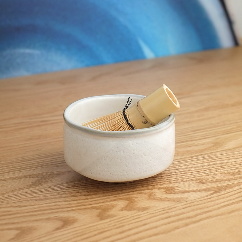 A traditional Japanese matcha tea set from Yamaman, including a Kohiki-style ceramic bowl with a rustic white glaze and a 100-prong bamboo whisk (chasen).
