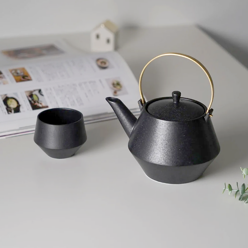 Yamatsu frustum japanese teapot in matte black with brass handle, shown beside matching black teacup.