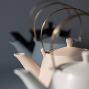 Yamatsu frustum japanese teapot in soft pink with brass handle, placed with matching teacup under natural light.