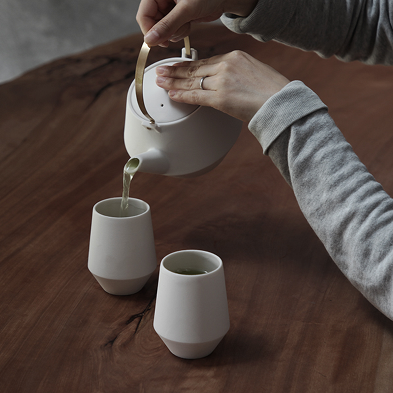 Pouring green tea from the pink Yamatsu Frustum teapot into matching cups on a wooden table.







