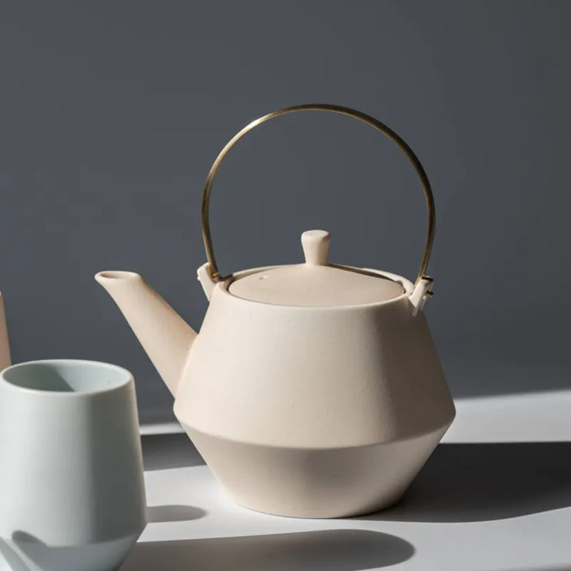Yamatsu Frustum Japanese teapot in matte pink with a matching teacup, featuring a modern angular design and brass handle.

