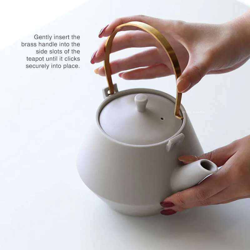 A person attaching the brass handle to a white Yamatsu Frustum Japanese teapot, showing the side slot mechanism.