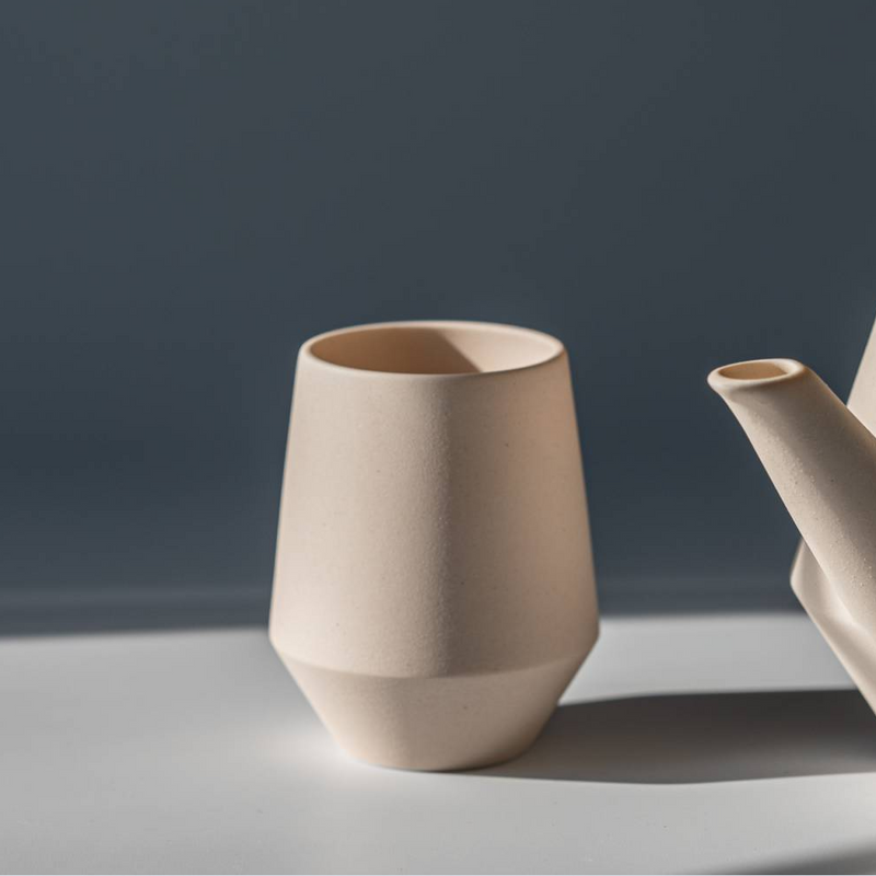 Close-up of Yamatsu Frustum Japanese teacup in matte pink finish beside matching teapot.

