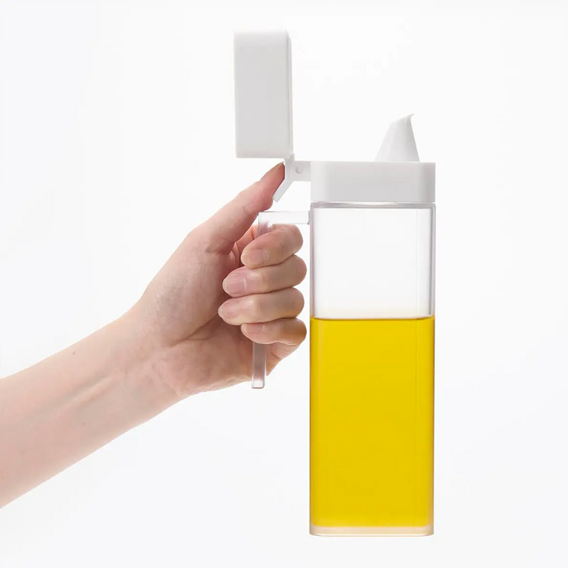 A hand holding the Yamazaki Tower dispenser and opening the white lid with a thumb to show its one-handed operation.

