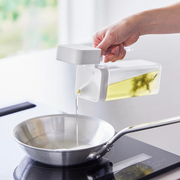 Pouring oil from the white Yamazaki Tower condiment dispenser into a frying pan during cooking.

