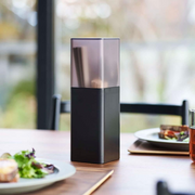 Yamazaki Tower Series Cutlery Stand in matte black with smoke transparent lid, shown on a dining table with chopsticks and cutlery stored upright inside.