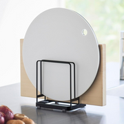 Yamazaki Tower black steel cutting board stand holding a white round cutting board and a rectangular wooden board upright on a kitchen bench.