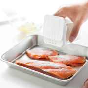 Yamazaki Tower flour and spice bottle in white sprinkling flour over salmon fillets on a tray