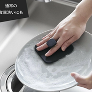 Person washing a ceramic plate with the black Yamazaki Tower Series silicone sponge in a kitchen sink.
