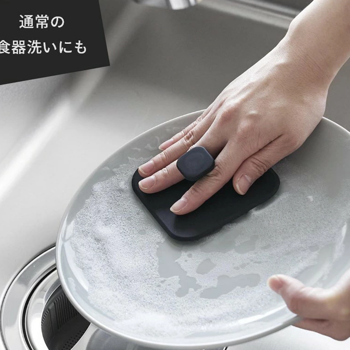 Person washing a ceramic plate with the black Yamazaki Tower Series silicone sponge in a kitchen sink.
