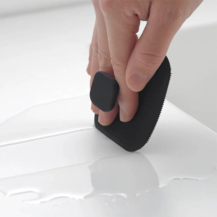 Close-up of a person using the Yamazaki Tower Series silicone sponge to clean a white tiled surface.
