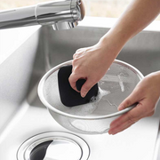 A lifestyle image showing the Yamazaki Tower Series Silicone Sponge being used to easily clean a mesh strainer in a kitchen sink.

