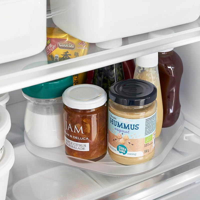 Yamazaki Tower Series Rotating Refrigerator Tray in white, shown inside a refrigerator shelf holding jam, hummus, and condiment bottles, demonstrating its practical storage use
