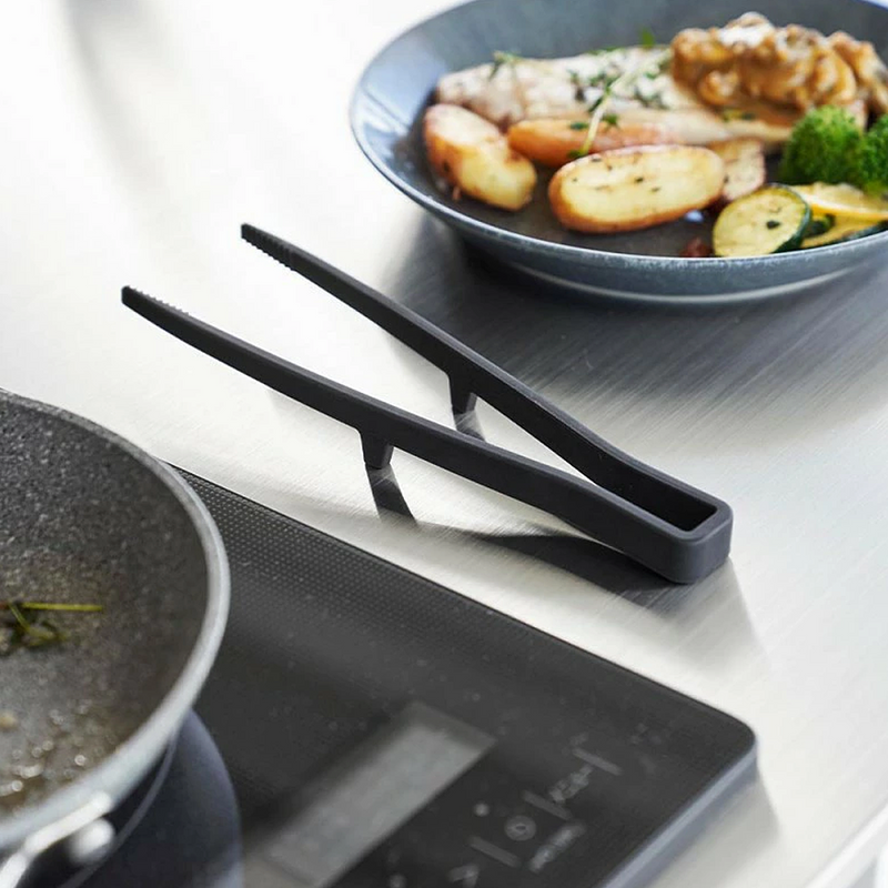 The Yamazaki Tower Series Small Silicone Tongs resting on their built-in stand on a countertop, keeping the tips elevated and the surface clean.

