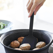Yamazaki Tower Series Silicone Small Turner flipping hamburger patties in a black frying pan.

