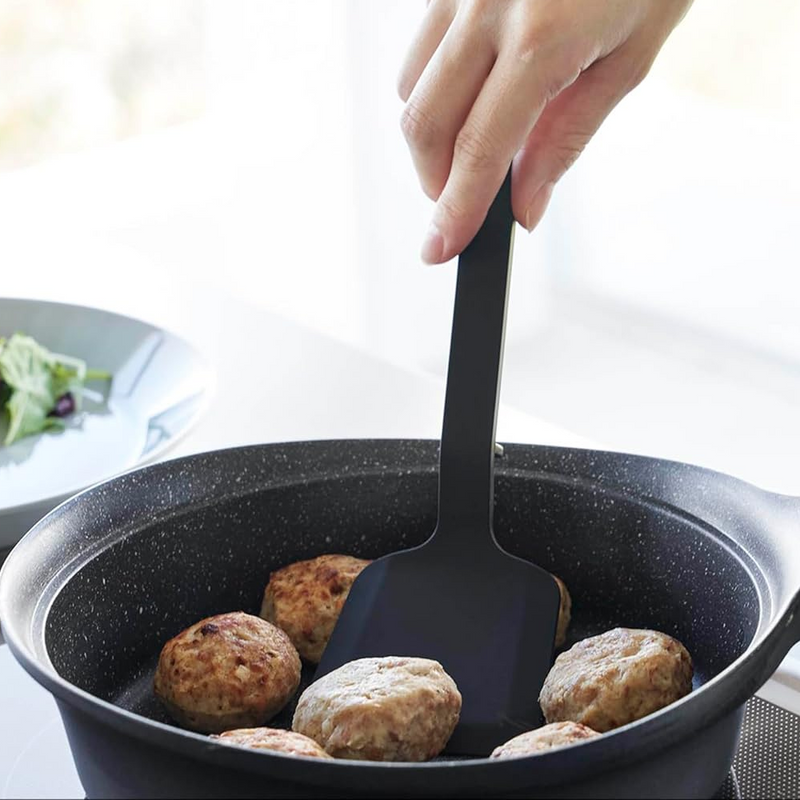 Yamazaki Tower Series Silicone Small Turner flipping hamburger patties in a black frying pan.

