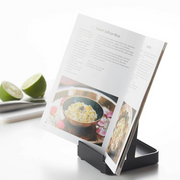 Yamazaki Tower Stand supporting an open cookbook, placed beside fresh limes and kitchen utensils.
