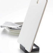 Yamazaki Tower Stand holding a white cutting board, displayed on a kitchen counter with plates and cutlery.
