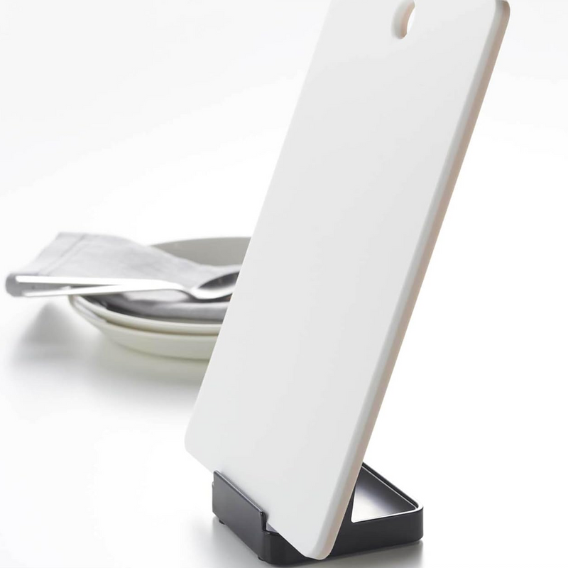 Yamazaki Tower Stand holding a white cutting board, displayed on a kitchen counter with plates and cutlery.
