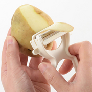 Person using a white potato peeler on a potato against a white background