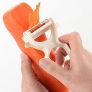 Hand using a carrot peeler on an orange carrot against a white background
