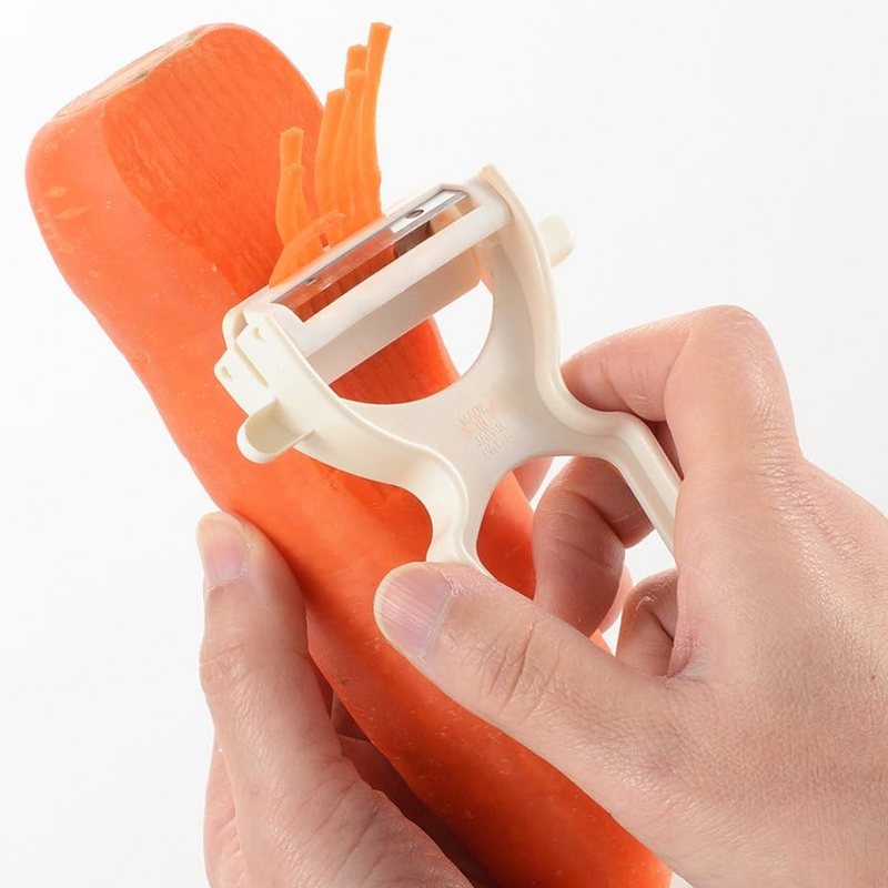 Hand using a carrot peeler on an orange carrot against a white background