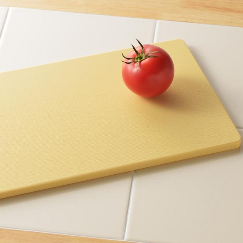 Red tomato on a yellow cutting board with a tiled kitchen floor background