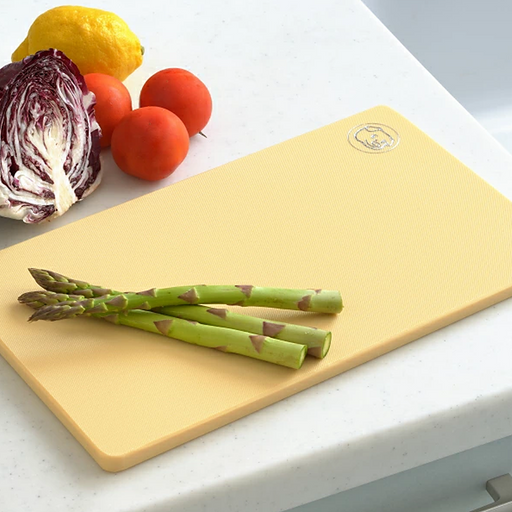 A yellow Yoshikawa antibacterial polyethylene cutting board with a textured surface, displayed with fresh asparagus and other vegetables.