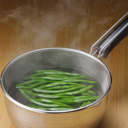 A person lifting the Yoshikawa strainer full of noodles out of a saucepan to drain the water.