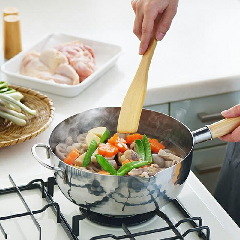 A person stirring a Japanese stew with carrots and snow peas in the Yoshikawa Yukihira saucepan on a gas stovetop.