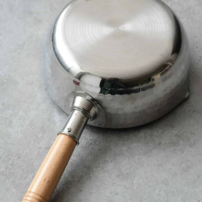 Metallic cooking pot with wooden handle on gray background