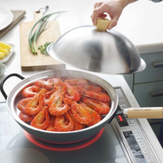 A Yoshikawa Cook-Pal Stainless Steel Steamer - 36cm filled with brightly cooked prawns, steaming on an induction cooktop. A hand is lifting the matching domed stainless steel lid off the steamer. In the background, there is a wooden cutting board with spring onions and a white plate with potatoes.