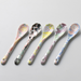 A set of 5 porcelain spoons with a delicate floral design, arranged on a white table.