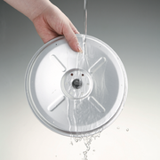 The easy-to-clean detachable inner lid from the Zojirushi MICOM Rice Cooker being rinsed under running water.

