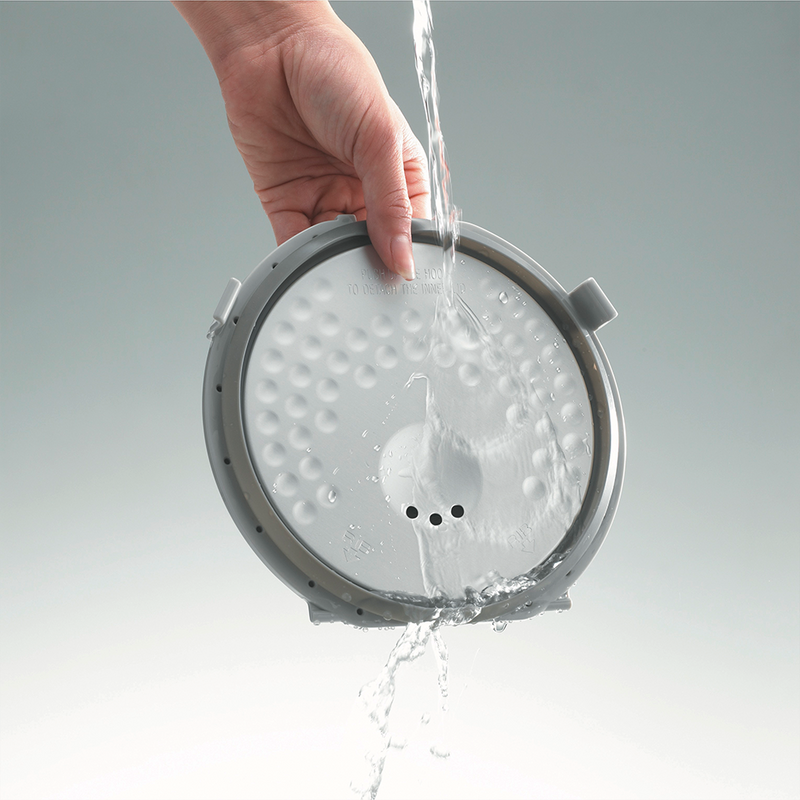 The detachable and washable inner lid of the Zojirushi Micom Rice Cooker being rinsed under a tap.

