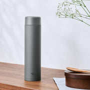 A matte grey Zojirushi SM-GA72 vacuum insulated flask standing on a wooden table next to a wooden container and spoon.