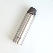 A silver Zojirushi SM-TA60-XA stainless steel vacuum insulated flask with a dark grey one-touch lid lying diagonally on a white background.