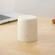 A beige Zojirushi SW-KA30 vacuum insulated food jar with a seamless one-piece lid sitting on a light wooden table.