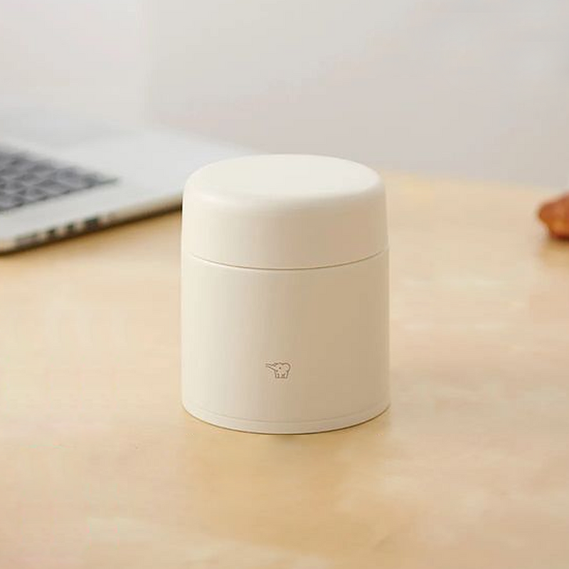 A beige Zojirushi SW-KA30 vacuum insulated food jar with a seamless one-piece lid sitting on a light wooden table.