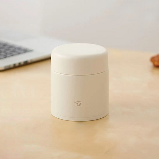 A beige Zojirushi SW-KA30 vacuum insulated food jar with a seamless one-piece lid sitting on a light wooden table.