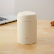 A beige Zojirushi SW-LA52 vacuum insulated food jar with a seamless one-piece lid sitting on a light wooden table.