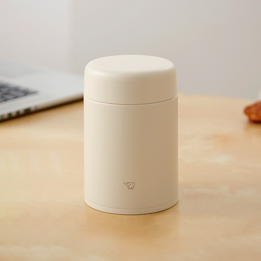 A beige Zojirushi SW-LA52 vacuum insulated food jar with a seamless one-piece lid sitting on a light wooden table.
