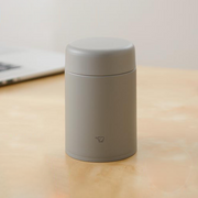 A matte grey Zojirushi SW-KA52 vacuum insulated food jar with a seamless one-piece lid sitting on a light wooden table.