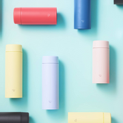 Various colourful Zojirushi flasks arranged on a light blue background.

