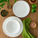 A flat lay of the Adam Liaw Everyday Noritake dinnerware set, showing the large plate, medium plate, and bowl placed on a wooden surface with green napkins and lime.
