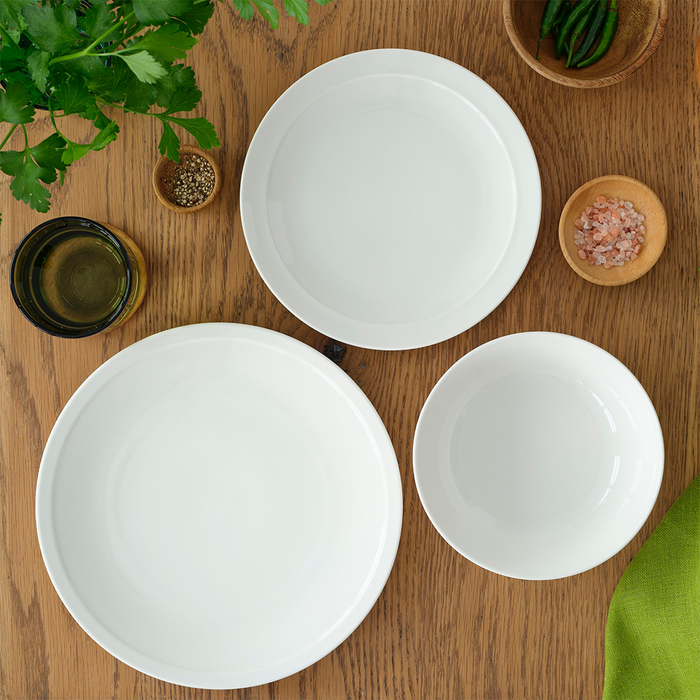 Another flat lay of the Adam Liaw Everyday Noritake dinnerware set, with a view of the large plate, medium plate, and bowl arranged on a table with green herbs and pink salt.