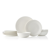 A collection of Adam Liaw Everyday Noritake dinnerware, including white porcelain plates and bowls, some stacked and some arranged with food.
